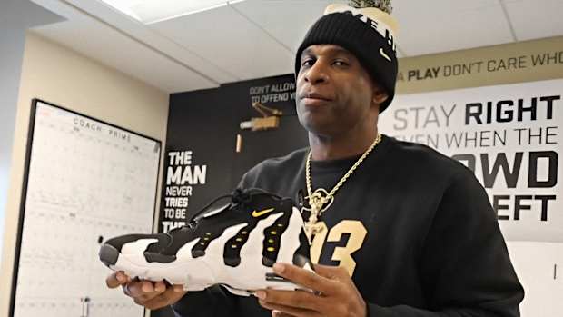 Deion Sanders holding Diamond Turf 3's in his office